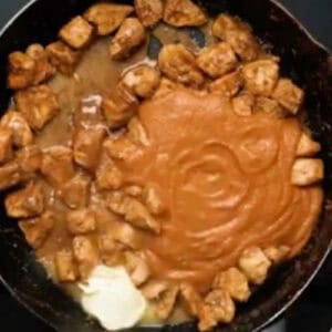 adding butter and butter chicken sauce to cooked chicken pieces in a skillet.