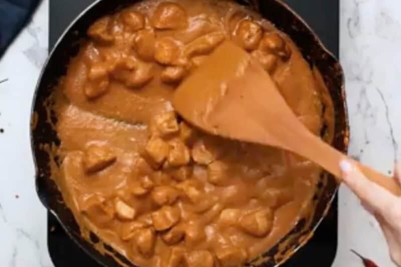 creamy butter chicken in a skillet with a wooden spatula.