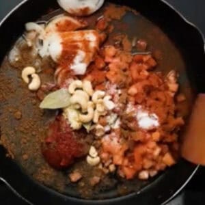 butter chicken sauce ingredients in a skillet with a wooden spatula.