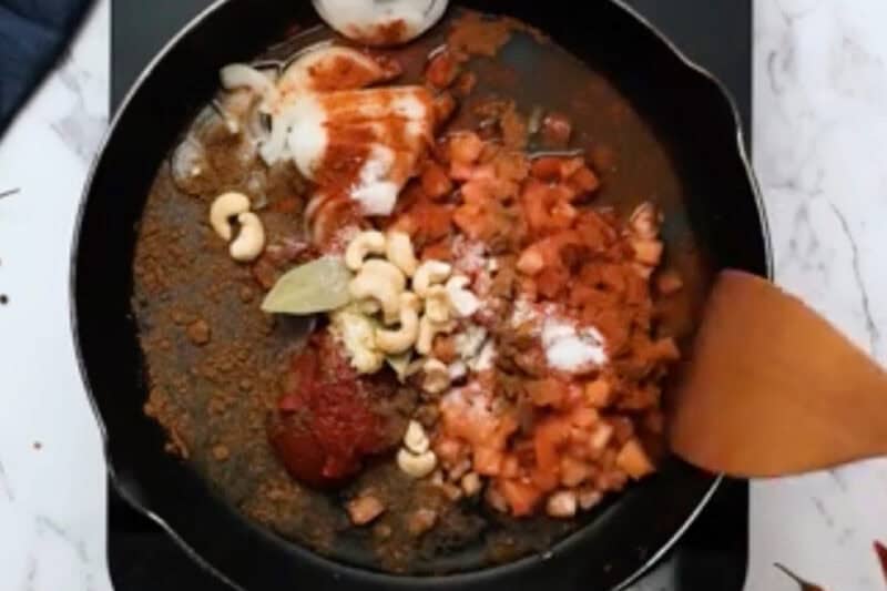 butter chicken sauce ingredients in a skillet with a wooden spatula.