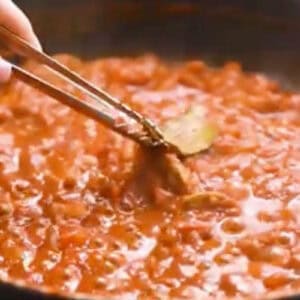 removing a bay leaf from butter chicken sauce with tongs.