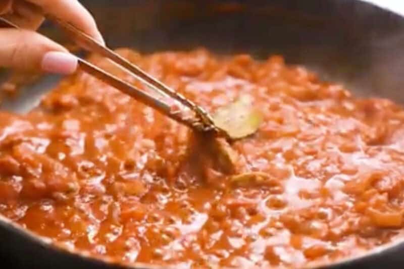 removing a bay leaf from butter chicken sauce with tongs.