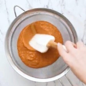 straining blended butter chicken sauce over a fine mesh sieve with a rubber spatula.