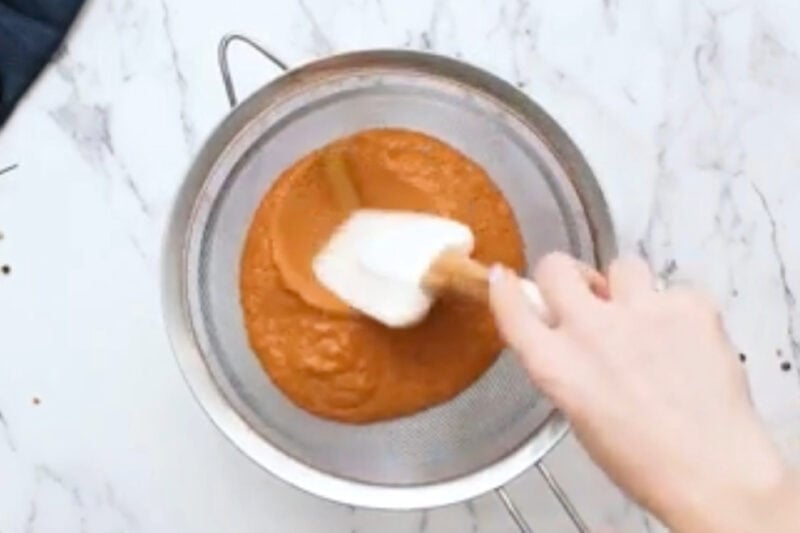 straining blended butter chicken sauce over a fine mesh sieve with a rubber spatula.