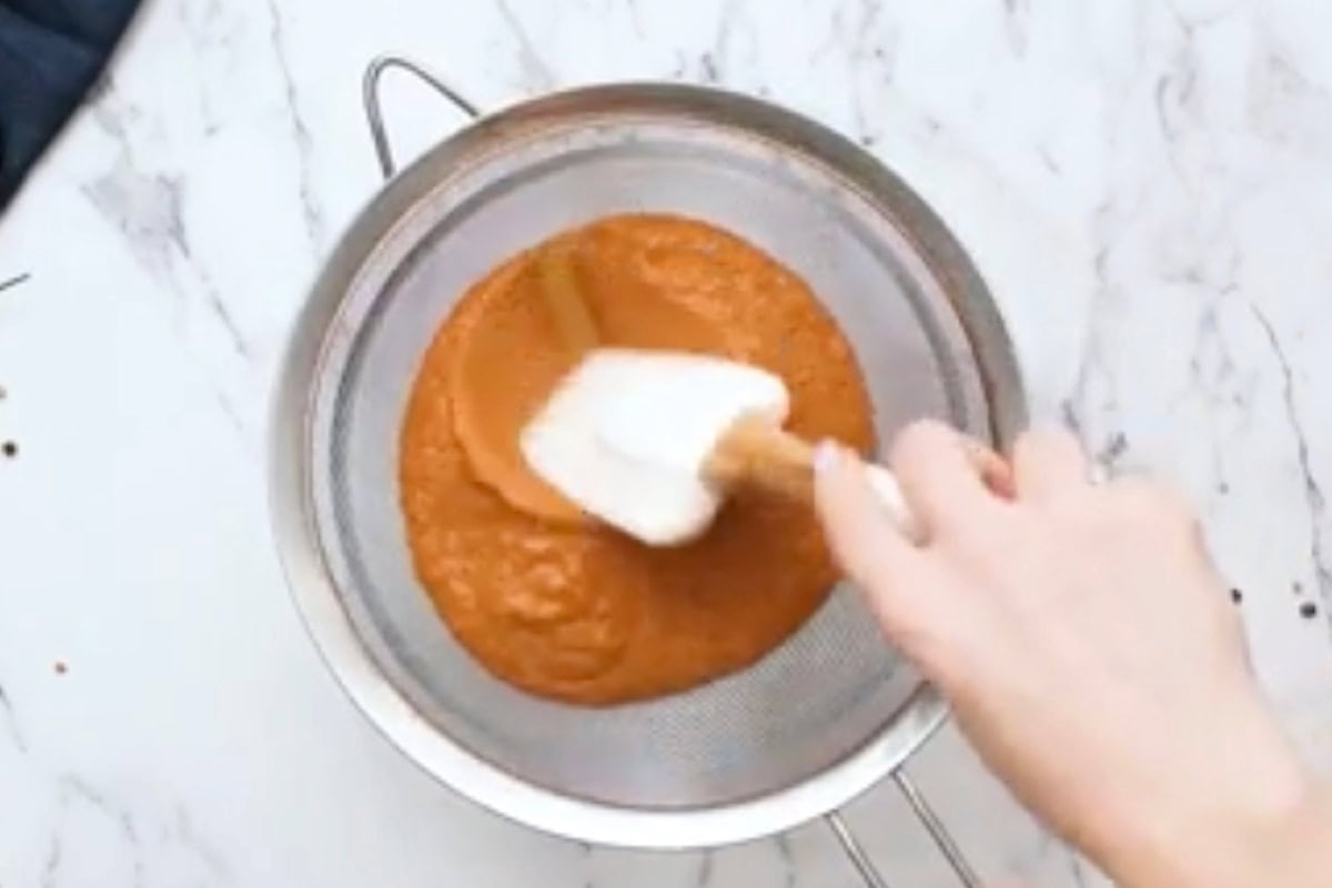straining blended butter chicken sauce over a fine mesh sieve with a rubber spatula.
