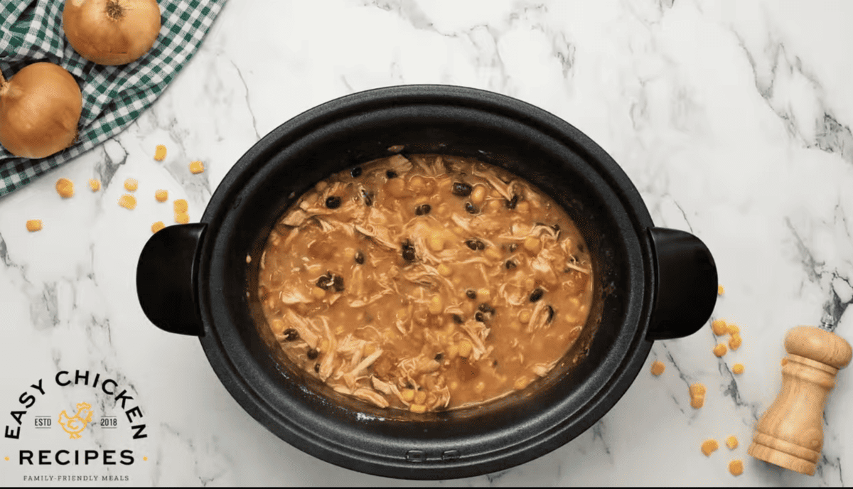 Cooked chicken enchilada soup is presented in a black Crockpot. 