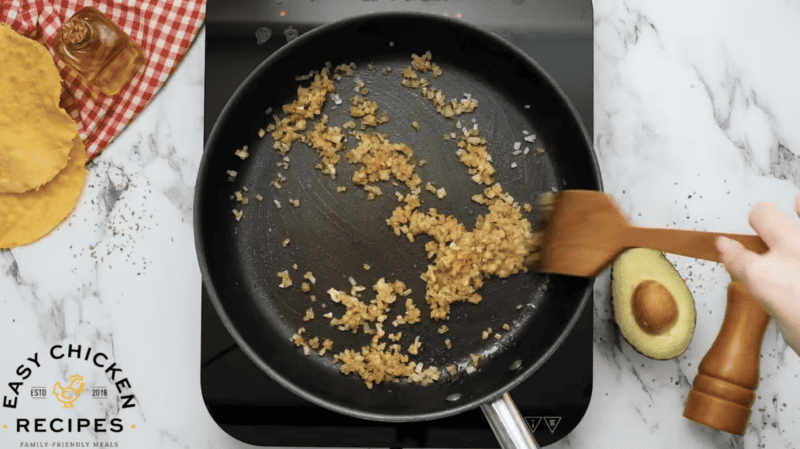 Onions, seasonings and garlic are being sautéed in a skillet.