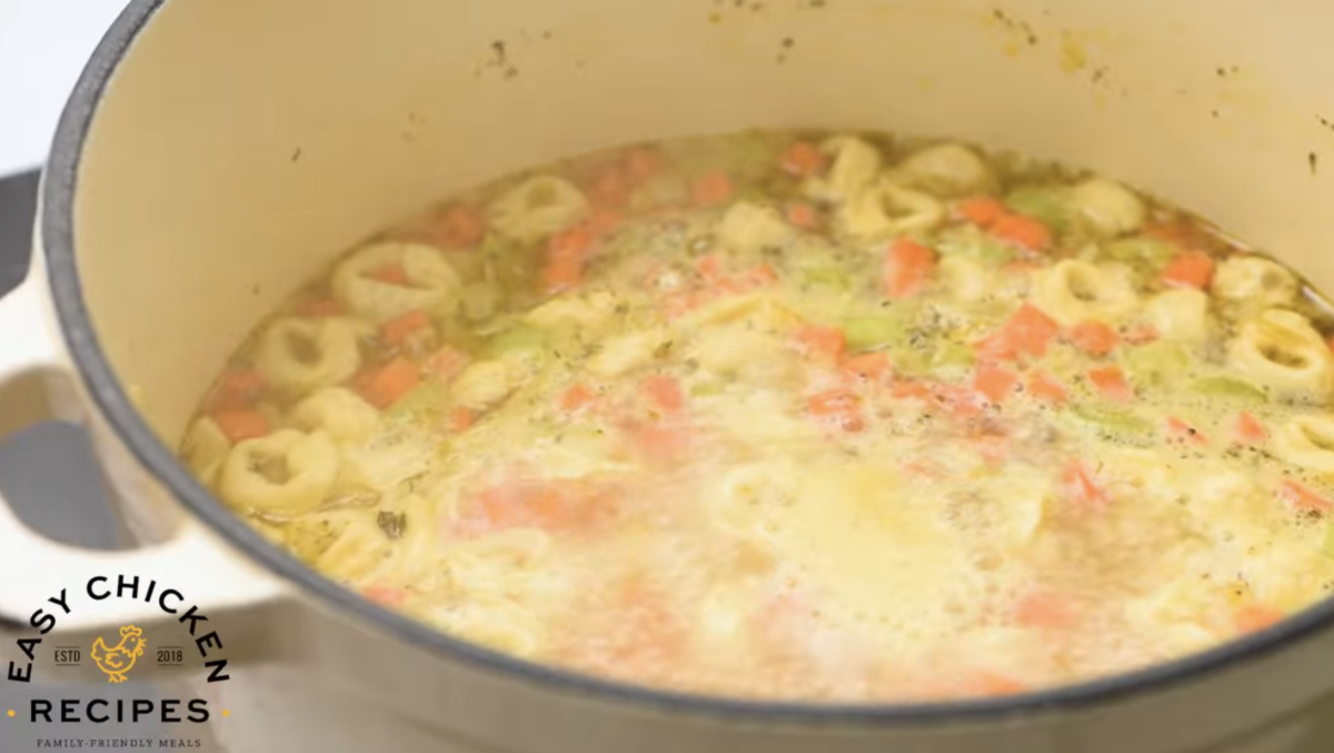 A dutch oven is filled with broth, tortellini and veggies. 