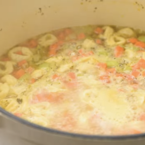 A dutch oven is filled with broth, tortellini and veggies.