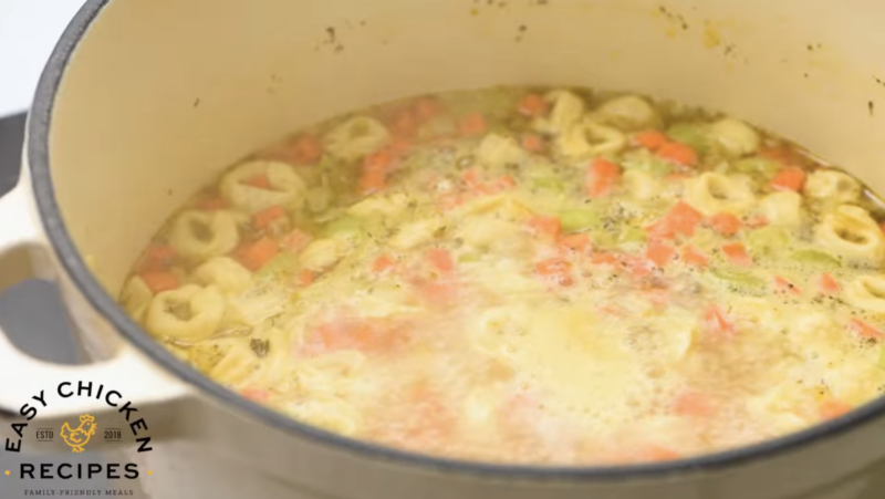 A dutch oven is filled with broth, tortellini and veggies.