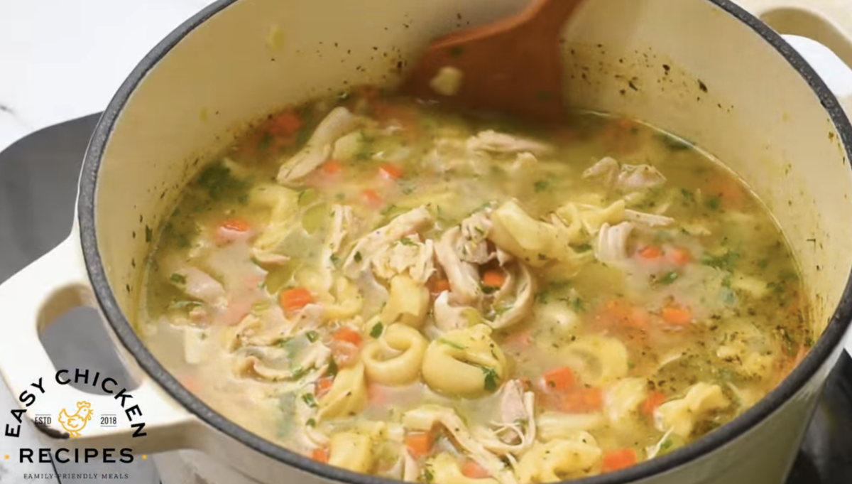 Chicken tortellini soup is being stirred in a large pot. 