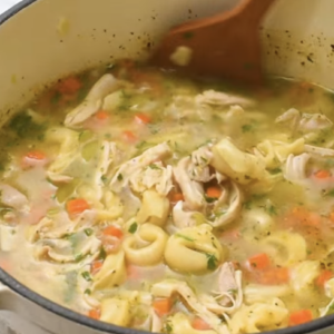 Chicken tortellini soup is being stirred in a large pot.