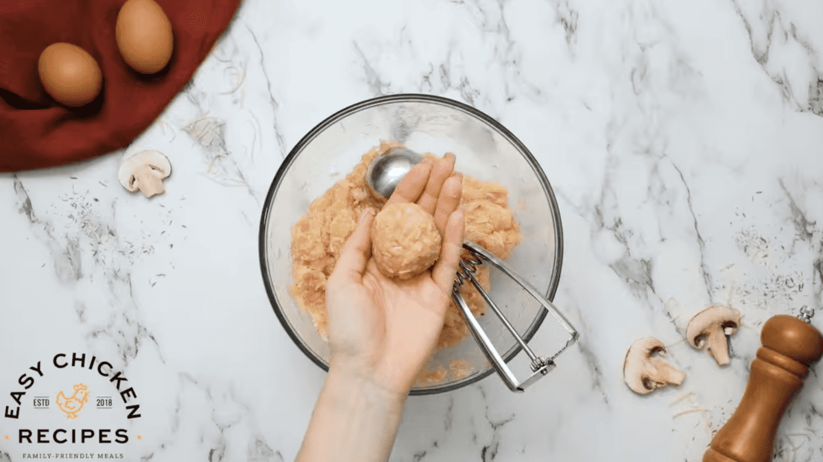 Chicken meatballs are being formed in a glass bowl. 