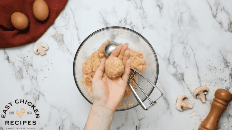 Chicken meatballs are being formed in a glass bowl.