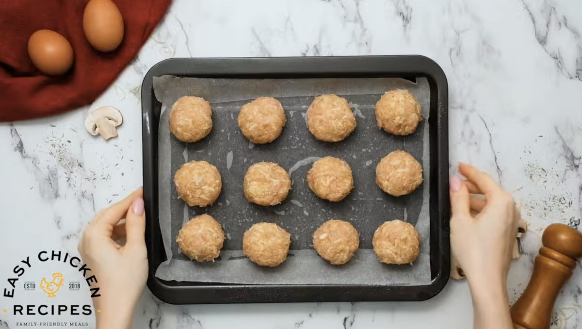 Uncooked meatballs are spread on a baking sheet. 