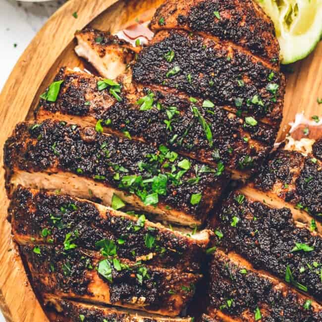 a plate of blackened chicken with a slice of cucumber.