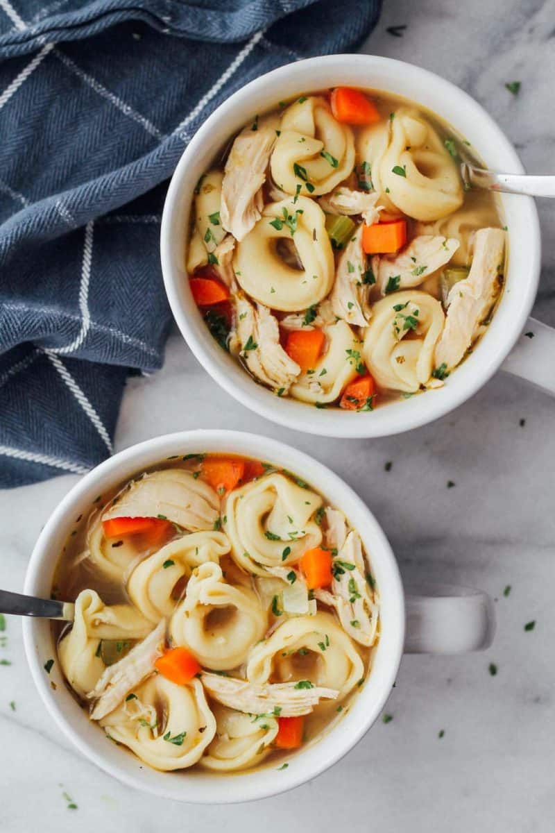Two bowls of chicken tortellini soup with carrots and noodles.