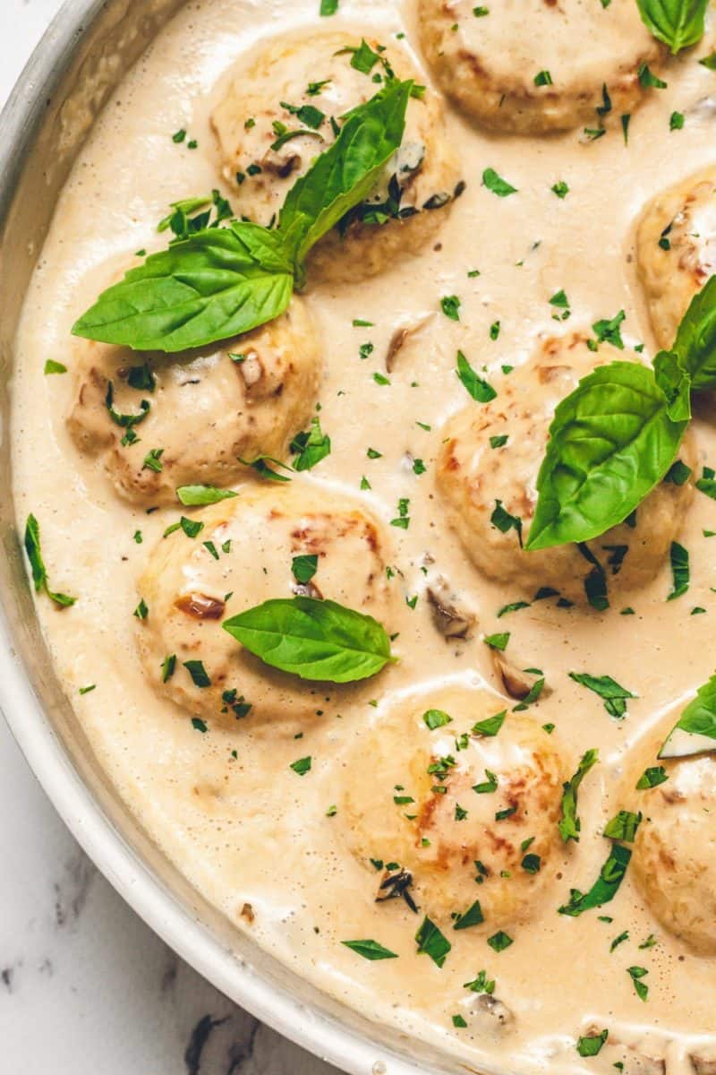Creamy chicken meatballs served with a savory sauce and garnished with fresh leaves.