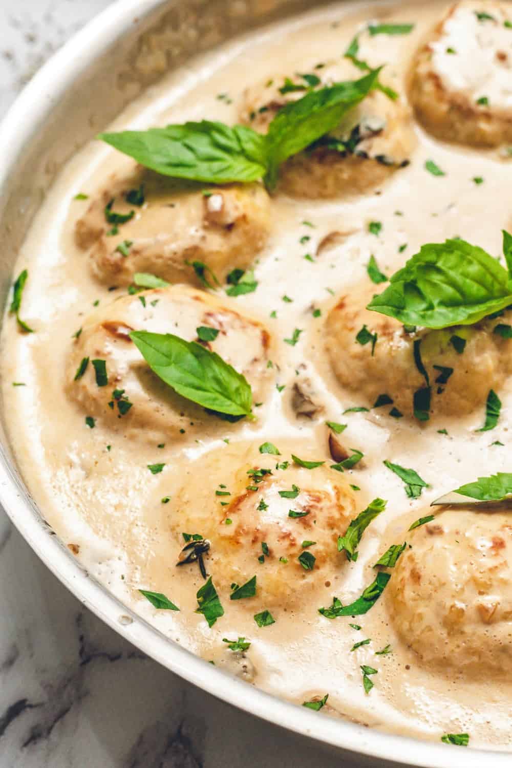Creamy Chicken Meatballs tossed in a skillet filled with pasta, sauce, and basil leaves.