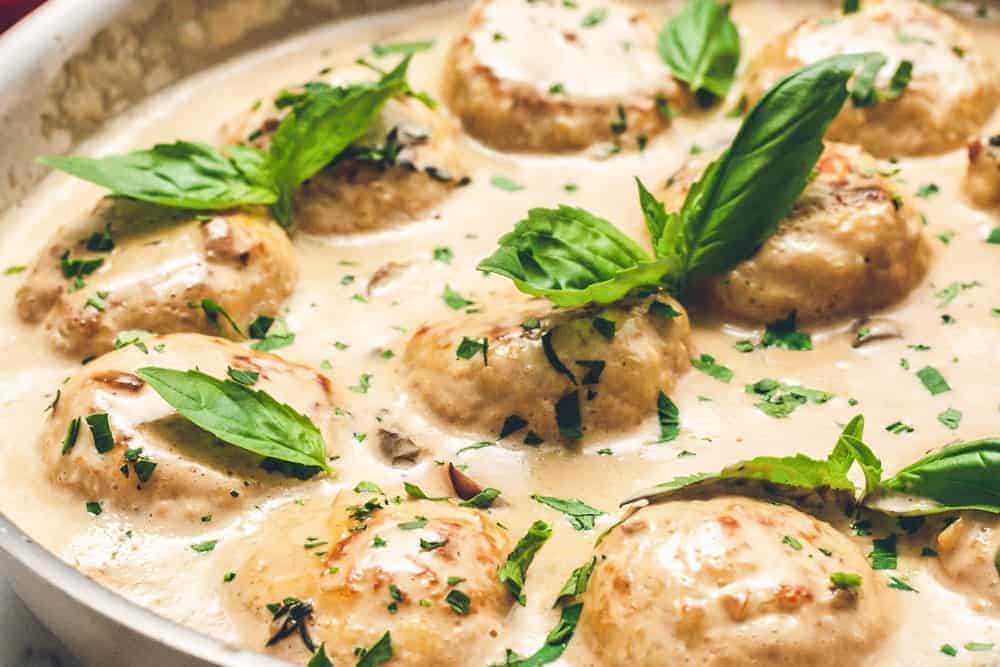 A plate of creamy chicken meatballs served with sauce and leaves.