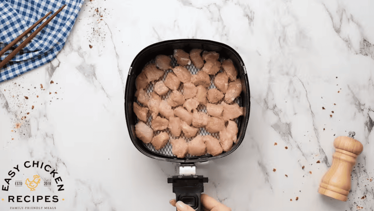 Raw chicken is spread across the basket of an air fryer. 