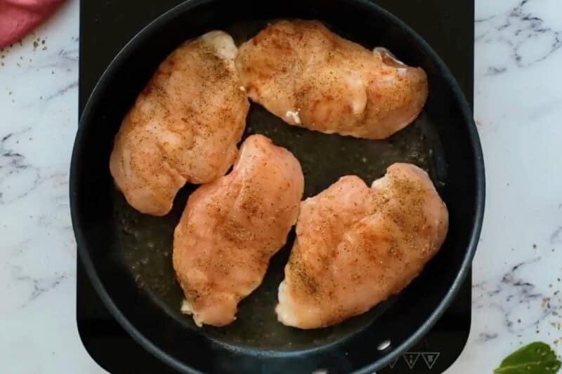searing four raw chicken breasts in a skillet.