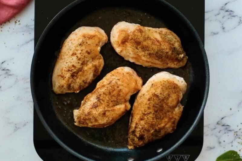 four seared seasoned chicken breasts in a skillet.