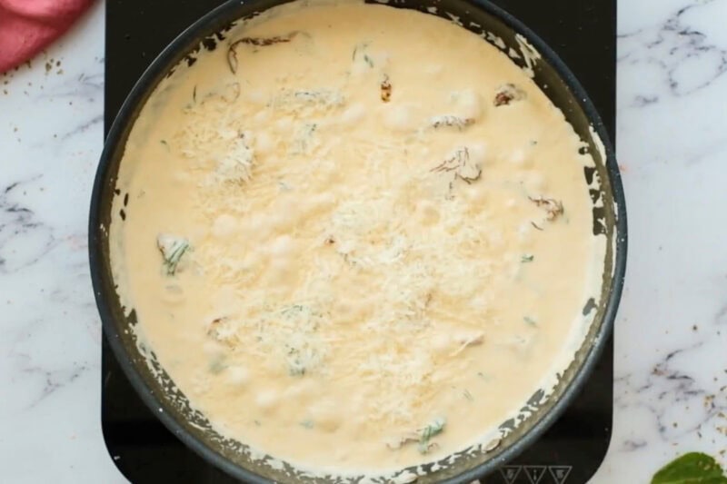 cheese added to creamy sun-dried tomato sauce in a skillet.