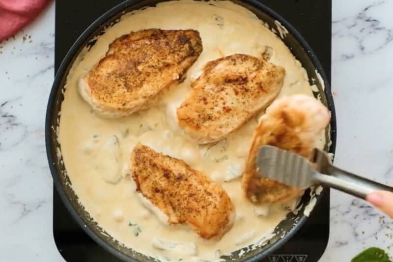adding cooked chicken to creamy sun-dried tomato sauce in a skillet.