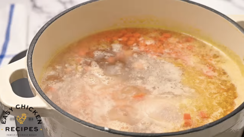 Chicken leg and broth are cooking with veggies in a pot.