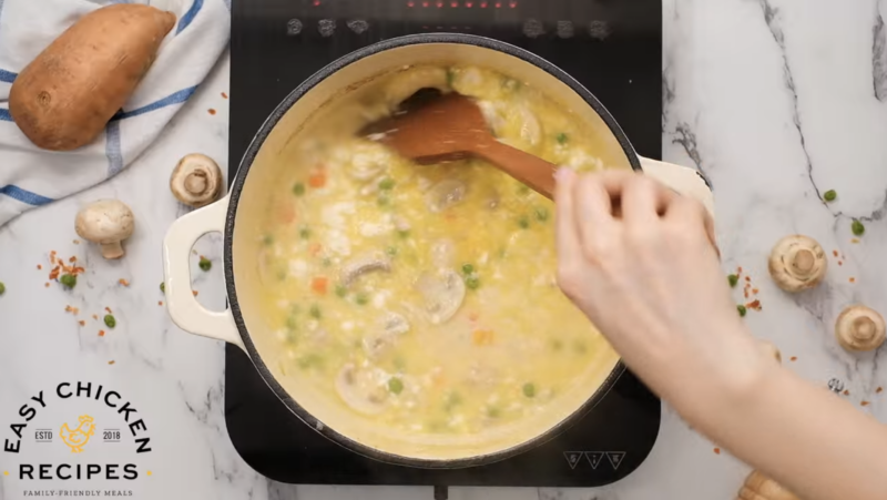 A pot of creamy chicken soup is being stirred.