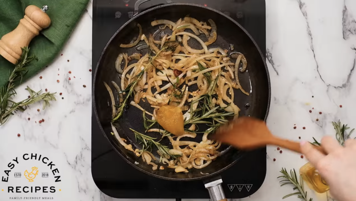 A person is frying onions in a pan to prepare Mustard Chicken.