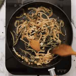 A person is frying onions in a pan to prepare Mustard Chicken.
