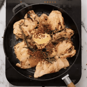Mustard chicken in a pan with herbs and spices.