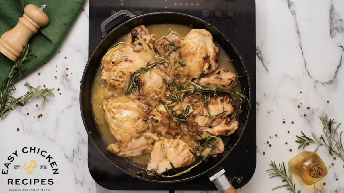 Mustard chicken sizzling in a skillet on a marble countertop.