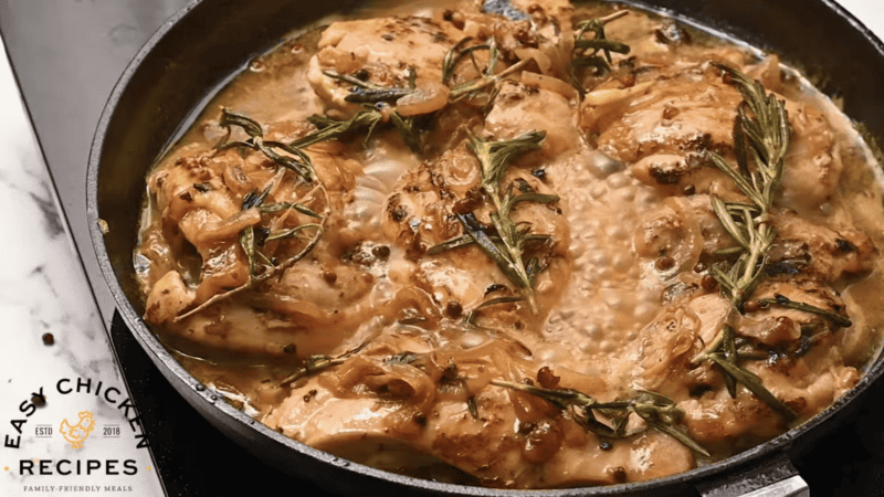 Mustard chicken with rosemary in a skillet on a stovetop.