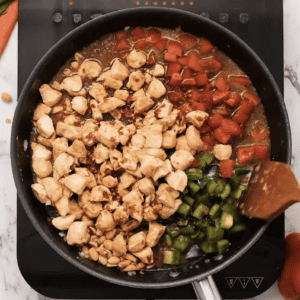 Chicken and vegetables are being cooked in a skillet.