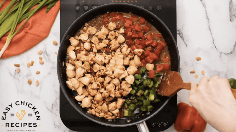 Chicken and vegetables are being cooked in a skillet.