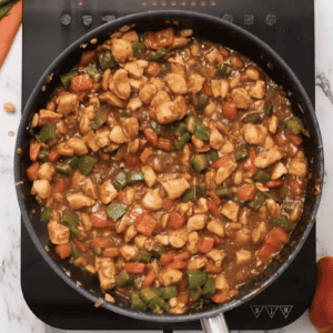 The sauce in the skillet has thickened with vegetables and chicken.