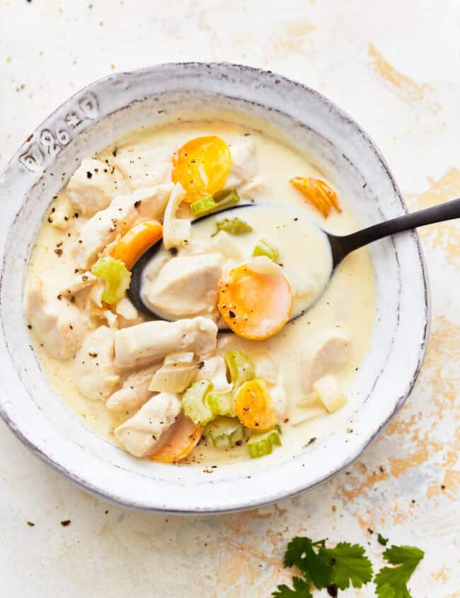 overhead view of a serving of creamy chicken soup in a white bowl with a spoon.