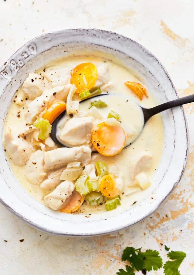 overhead view of a serving of creamy chicken soup in a white bowl with a spoon.