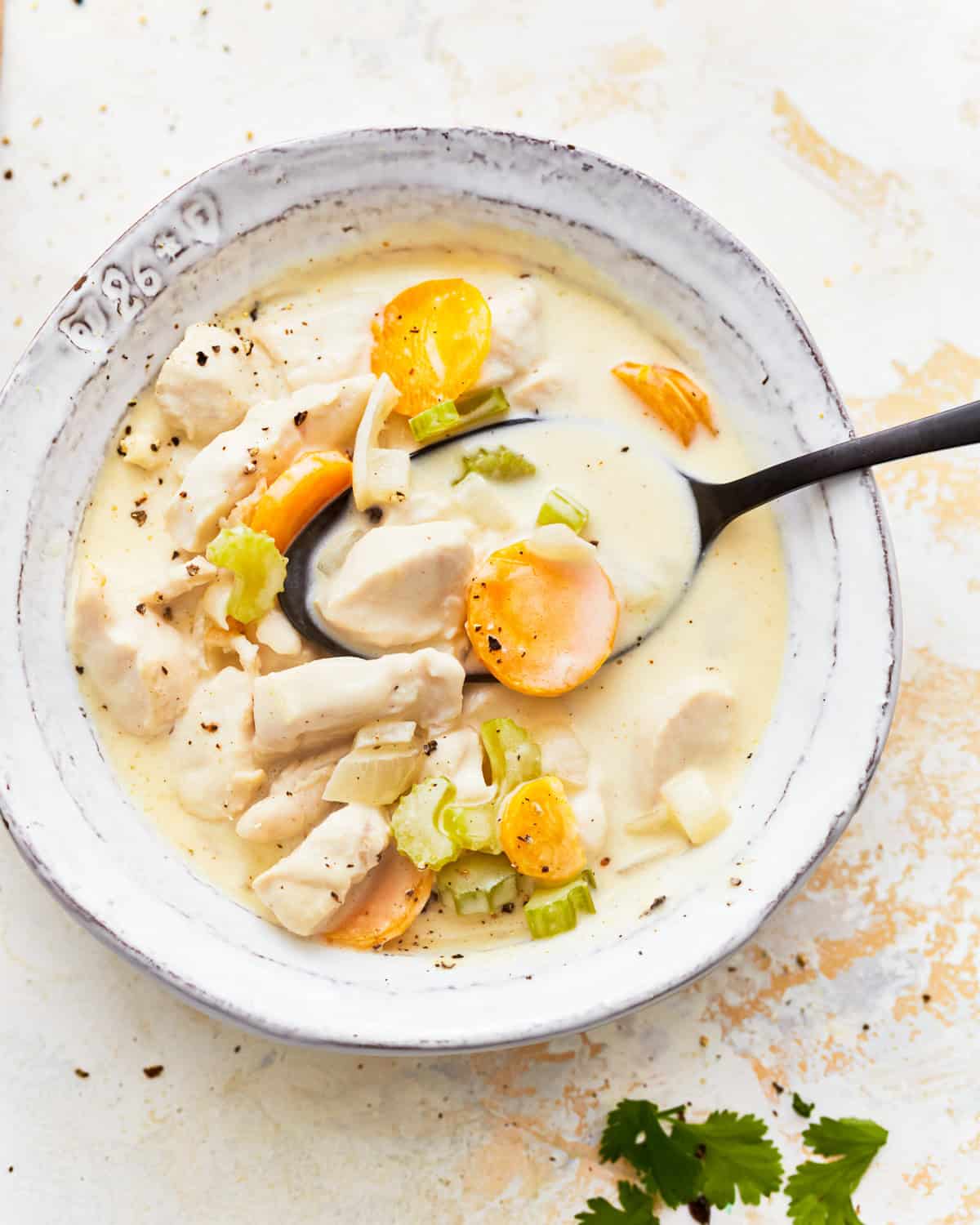 overhead view of a serving of creamy chicken soup in a white bowl with a spoon.