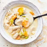 overhead view of a serving of creamy chicken soup in a white bowl with a spoon.