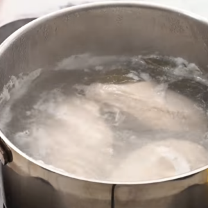 Chicken breasts are boiling in a pot.