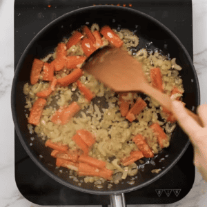 A person stirs vegetables in a frying pan.