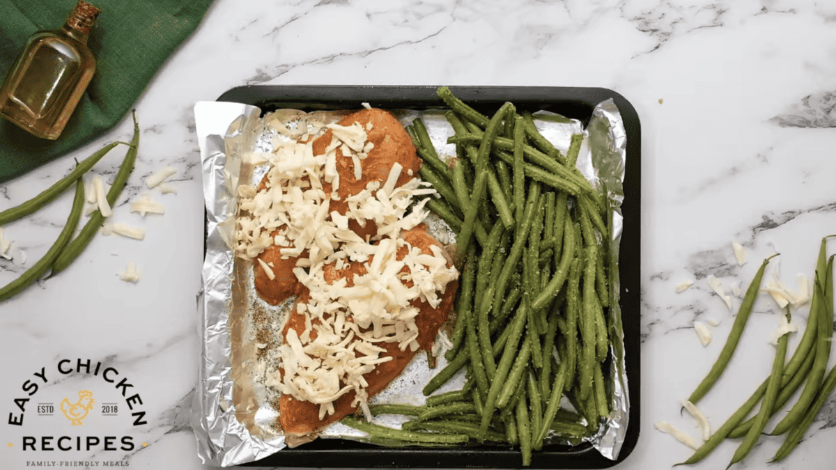 Chicken coated with chicken is placed next to green beans on a sheet pan. 