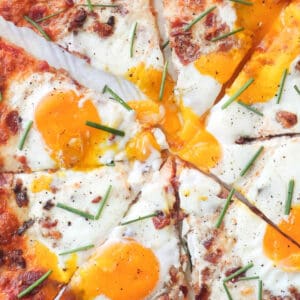 cropped overhead view of a sliced breakfast pizza topped with sunny side up eggs and chives.