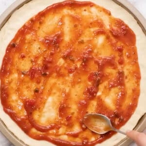 spreading pizza sauce over pizza dough in a pizza pan.