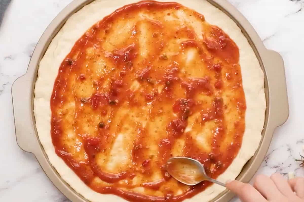 spreading pizza sauce over pizza dough in a pizza pan.