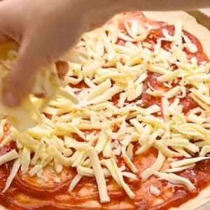 sprinkling shredded cheese over pizza sauce. on dough.